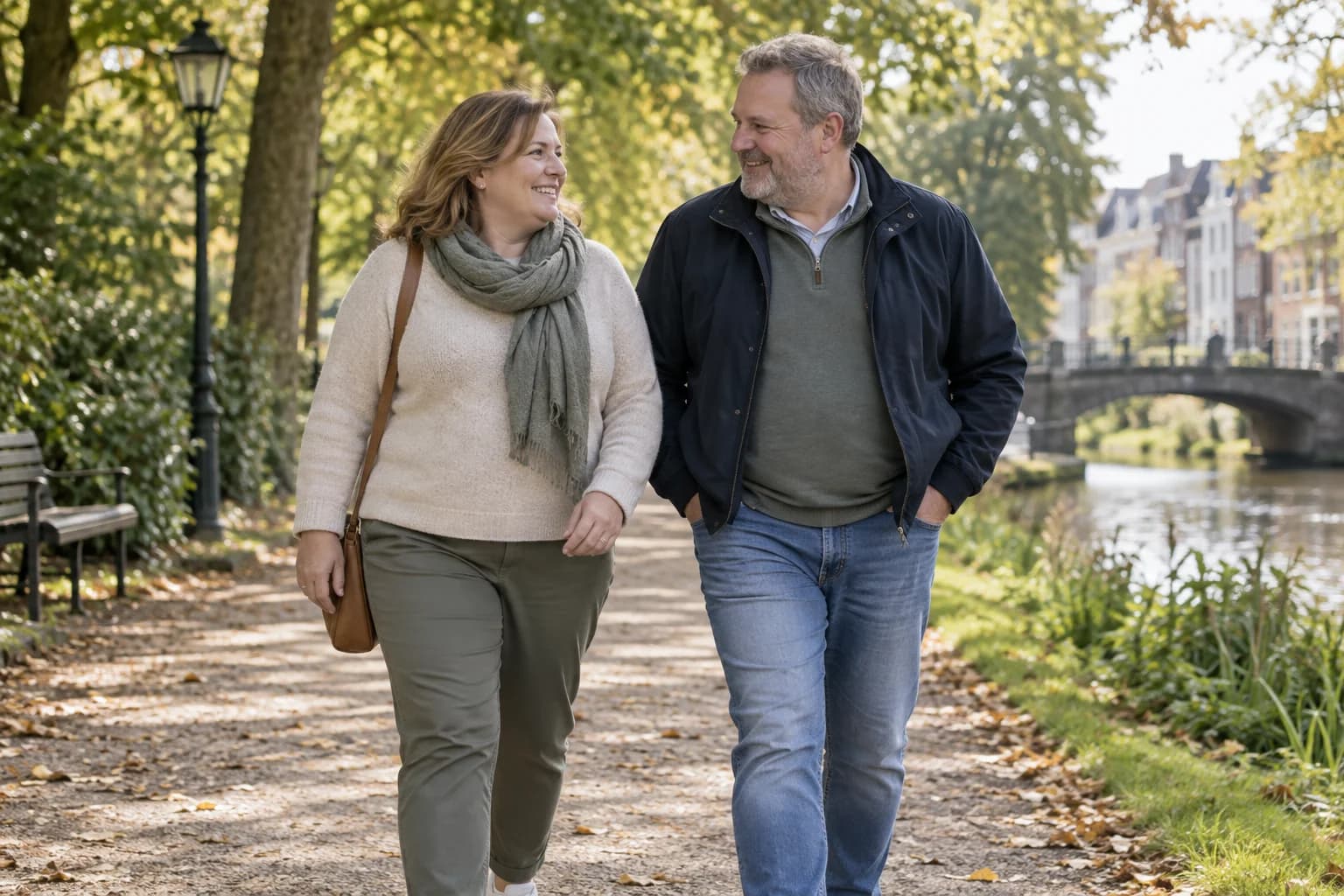 Twee volwassenen wandelen samen langs het water in een Nederlands park.